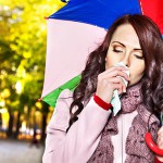 Frau mit Regenschirm und Taschentuch erkrankt an Erkältung