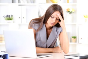 Eine Bürokauffrau mit Kopfschmerzen an ihrem Arbeitsplatz